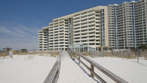En strandpromenade der fører hen til et højt hotel med mange altaner.