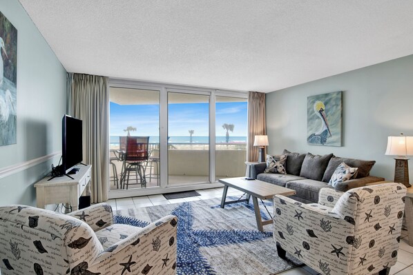 A hotel room with a balcony, a sofa, a TV, and a painting.