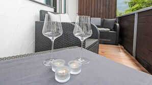 A balcony with two wicker sofas, a table with four wine glasses and candles, and a view of greenery and mountains in the background. - Am Birkenhain by Interhome (Seefeld in Tirol)