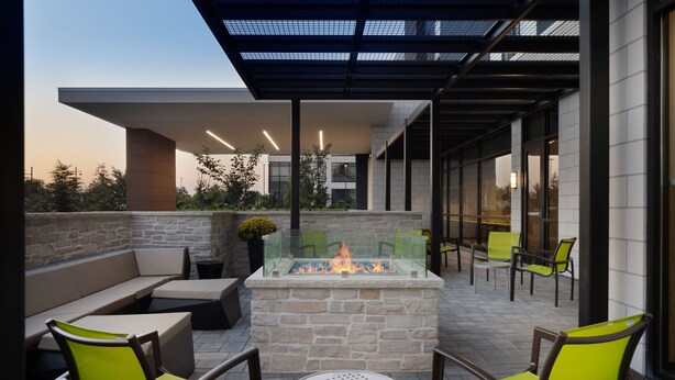 An outdoor patio area with a stone fire feature, seating, and a glass-top table. - SpringHill Suites by Marriott Bowling Green (Bowling Green)