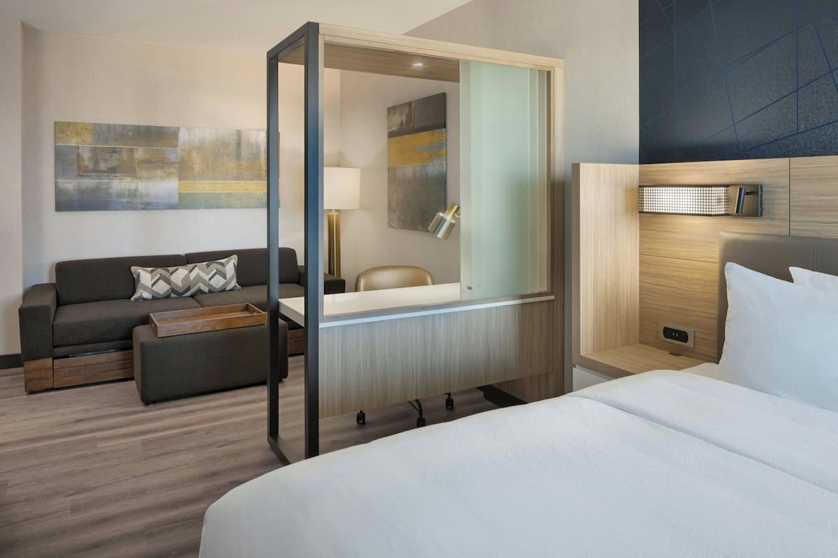 A modern hotel room with a large bed, a sofa, a small table, and a mirror.
