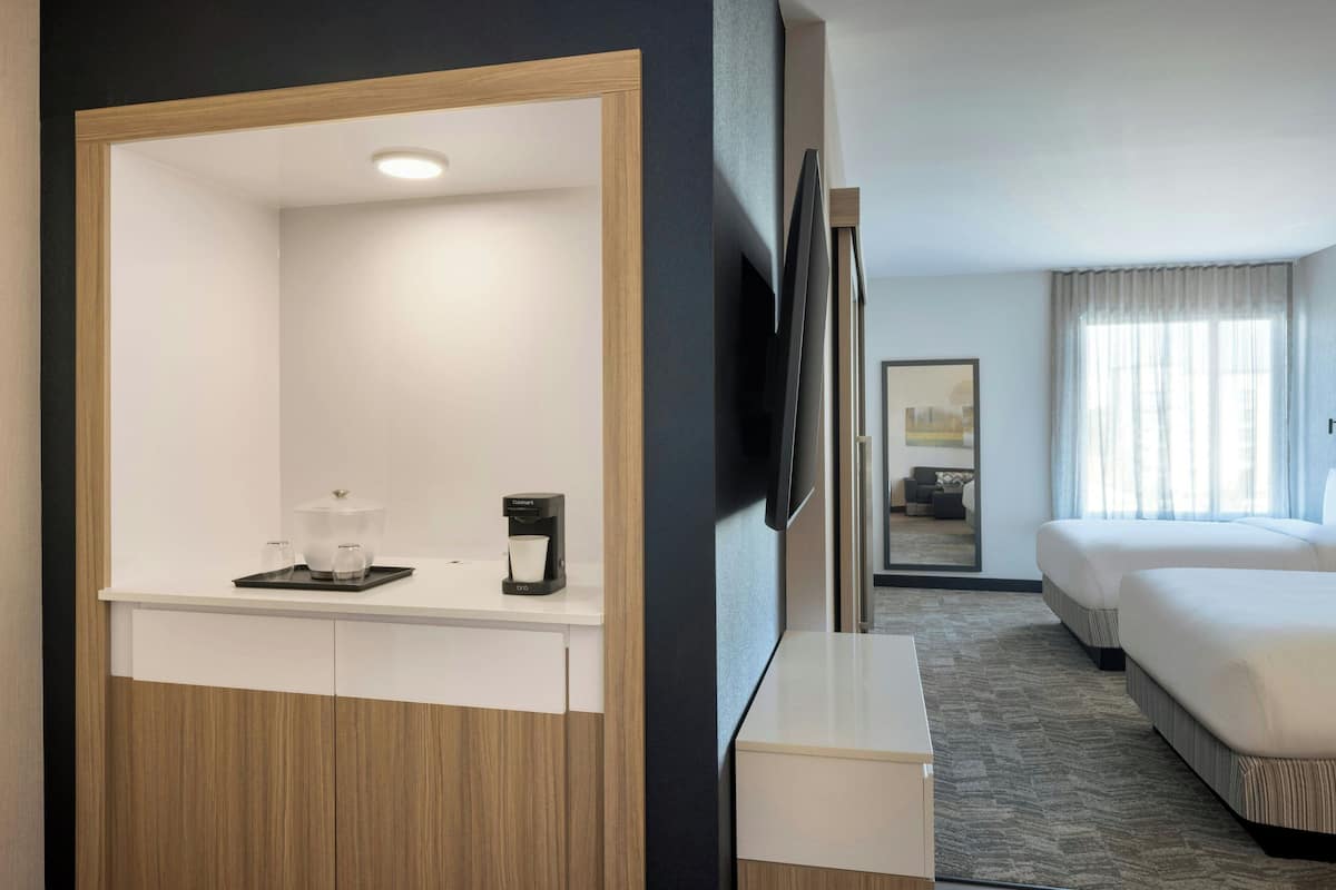 A hotel room with a wooden wardrobe, a coffee station, a flat-screen TV, a bed, and a window with curtains.
