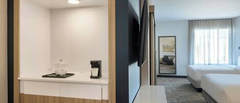 A hotel room with a wooden wardrobe, a coffee station, a flat-screen TV, a bed, and a window with curtains.