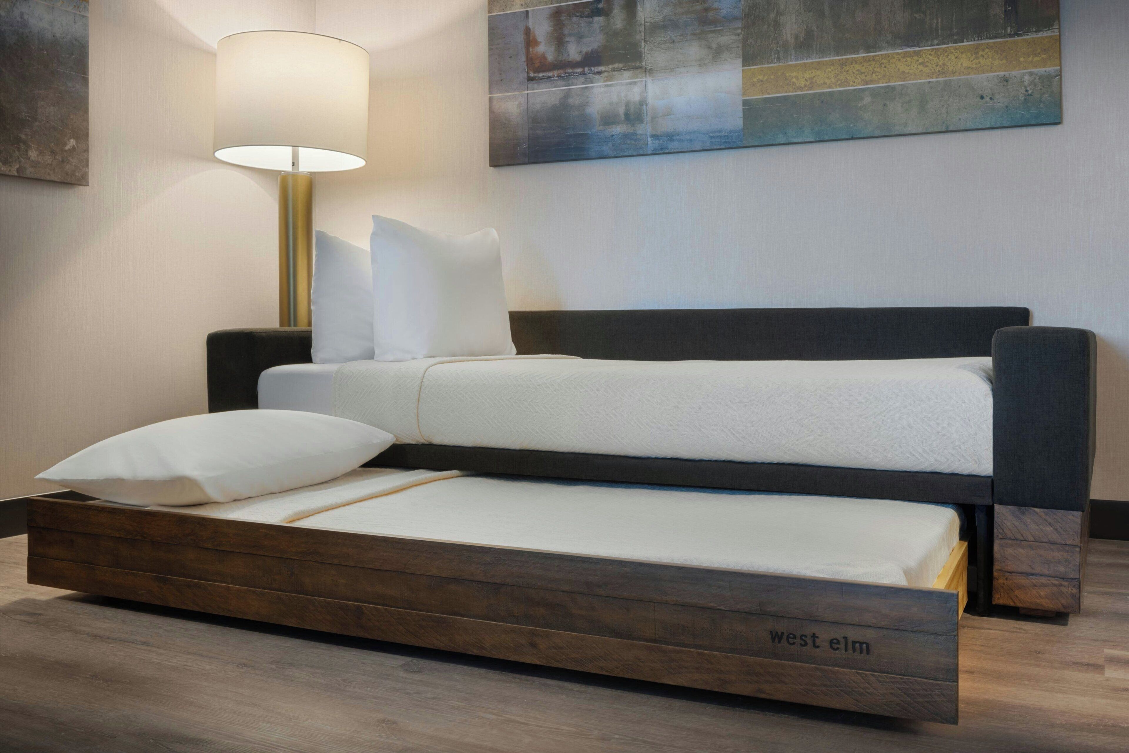 Una cama moderna con estructura de madera y cabecera, acompañada de una mesita de noche y una lámpara.