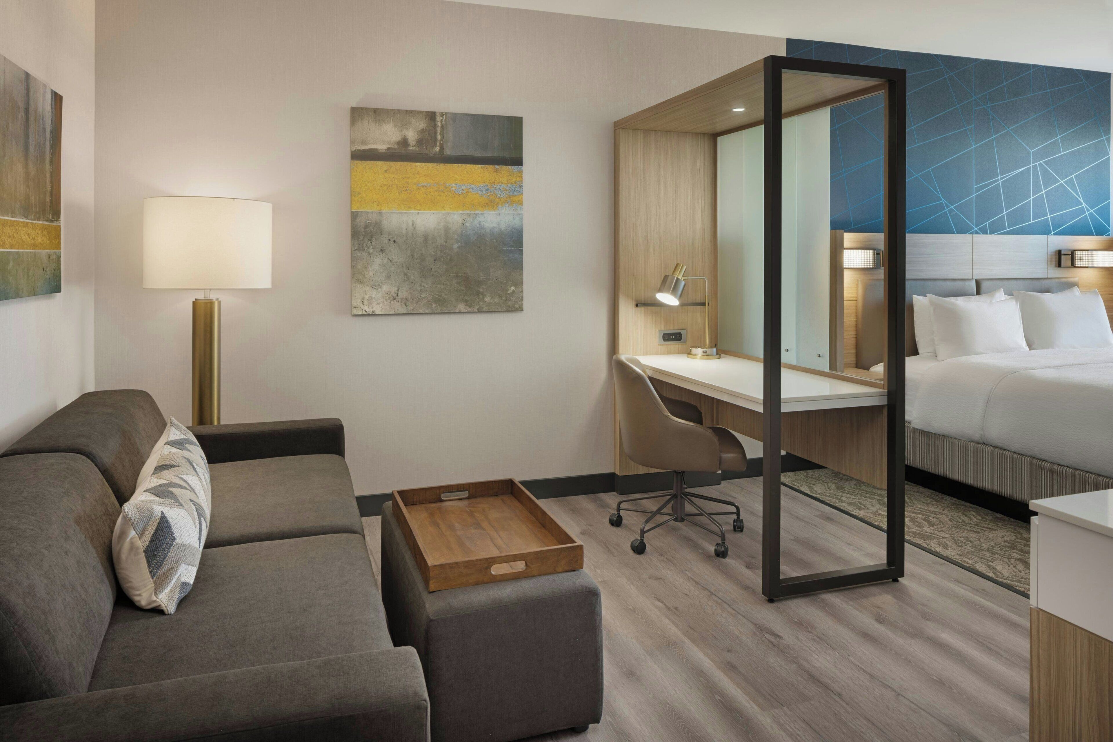 A modern hotel room with a sofa, desk, and bed.