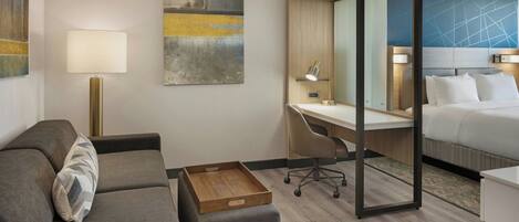 A modern hotel room with a sofa, desk, and bed.