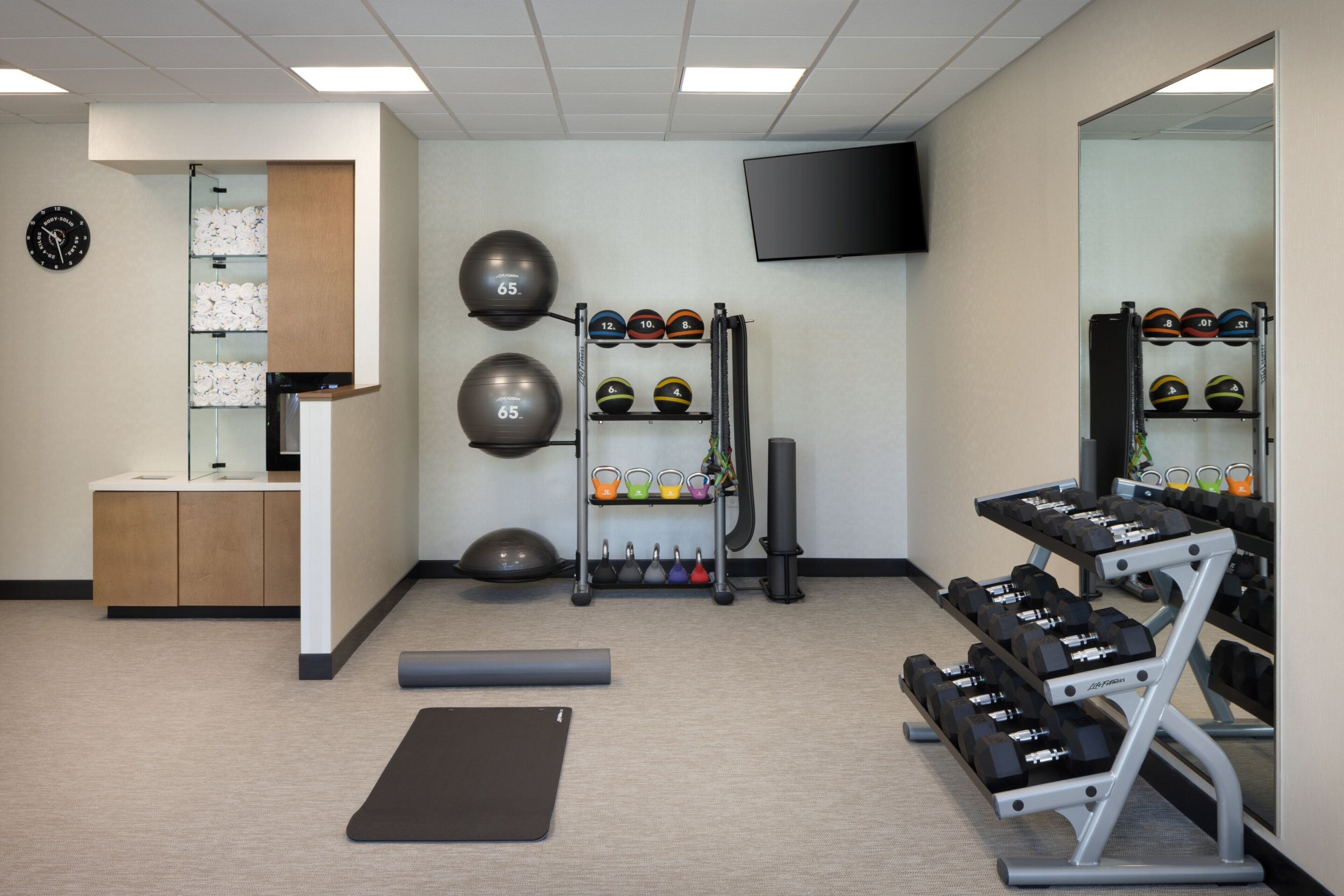 Een sportschool met trainingsapparatuur, een spiegel en een televisie aan de muur.
