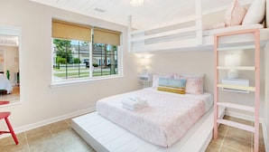 Une chambre avec un lit superposé, une fenêtre donnant sur l’extérieur, une table de chevet avec une lampe et un lit recouvert d’une couverture rose.