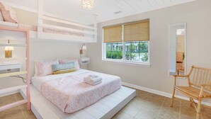 A bedroom with a bunk bed, a single bed, a bedside table, a lamp, a chair, and a window with a view of greenery. - Salt Gypsy Unit A Expansive Outdoor Space w Pool (Tybee Island)