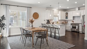 Une cuisine moderne avec des meubles blancs, un îlot central et un coin repas comprenant une table et des chaises en bois.