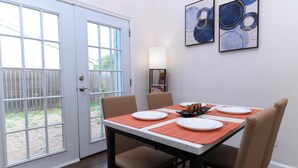 Un coin repas avec une table dressée pour quatre personnes, des chaises, une porte avec des panneaux de verre et deux tableaux abstraits accrochés au mur.