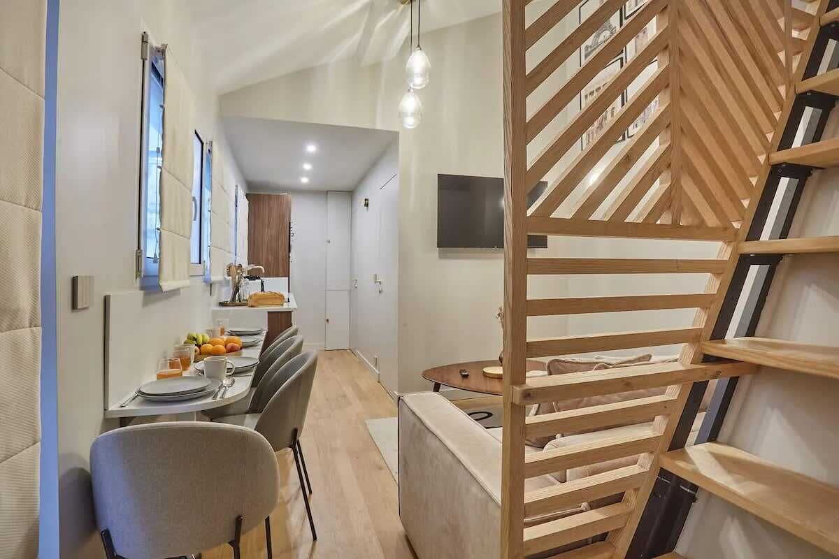 A modern kitchen with a dining area, wooden staircase, and a TV mounted on the wall.