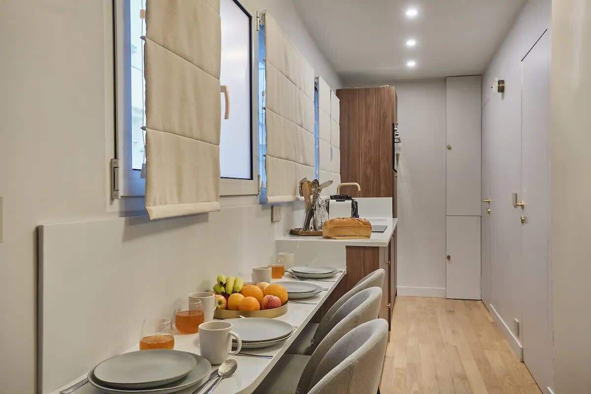 Een moderne keuken met witte kastjes, een houten aanrecht en een eethoek met een tafel gedekt voor twee personen.