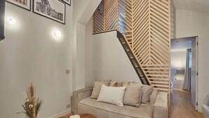 A modern living room with a sofa, a wooden coffee table, and a decorative vase. A staircase with a wooden railing leads to another room. - Place de la Bastille Cozy and Modern 2BD (Paris)