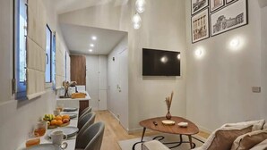 A modern living room with a dining area, a flat-screen TV mounted on the wall, and a small round table with a vase. - Place de la Bastille Cozy and Modern 2BD (Paris)