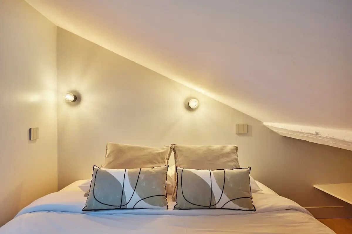 Un dormitorio con cama, dos lámparas de noche y techo inclinado.