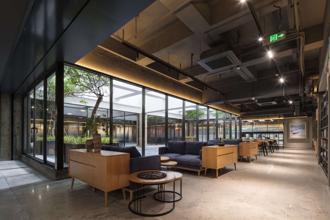 A modern interior with glass walls, a seating area with sofas and tables, and a visible exit sign.