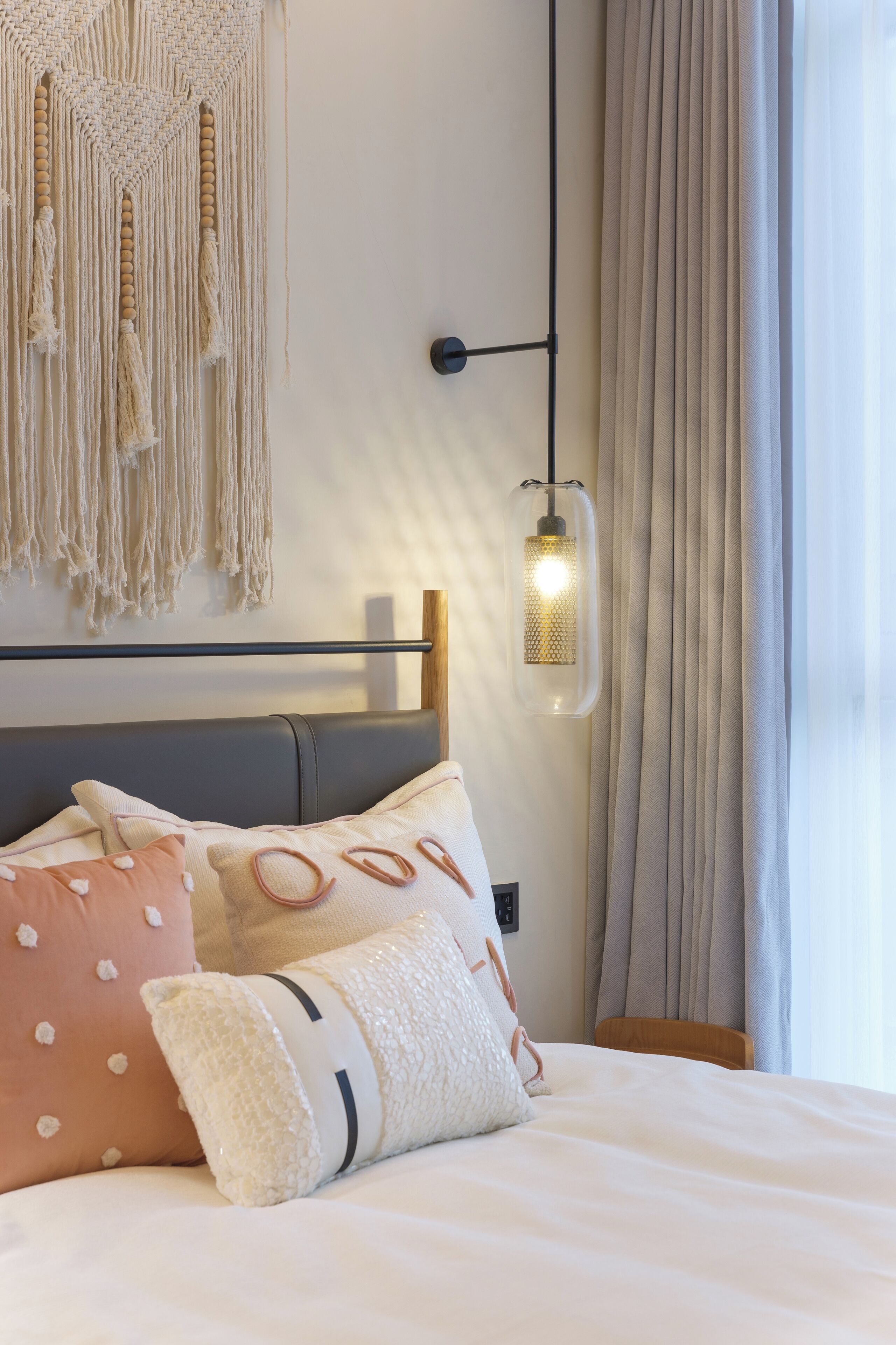 A neatly made bed with decorative pillows, a macrame wall hanging, and a hanging light fixture.