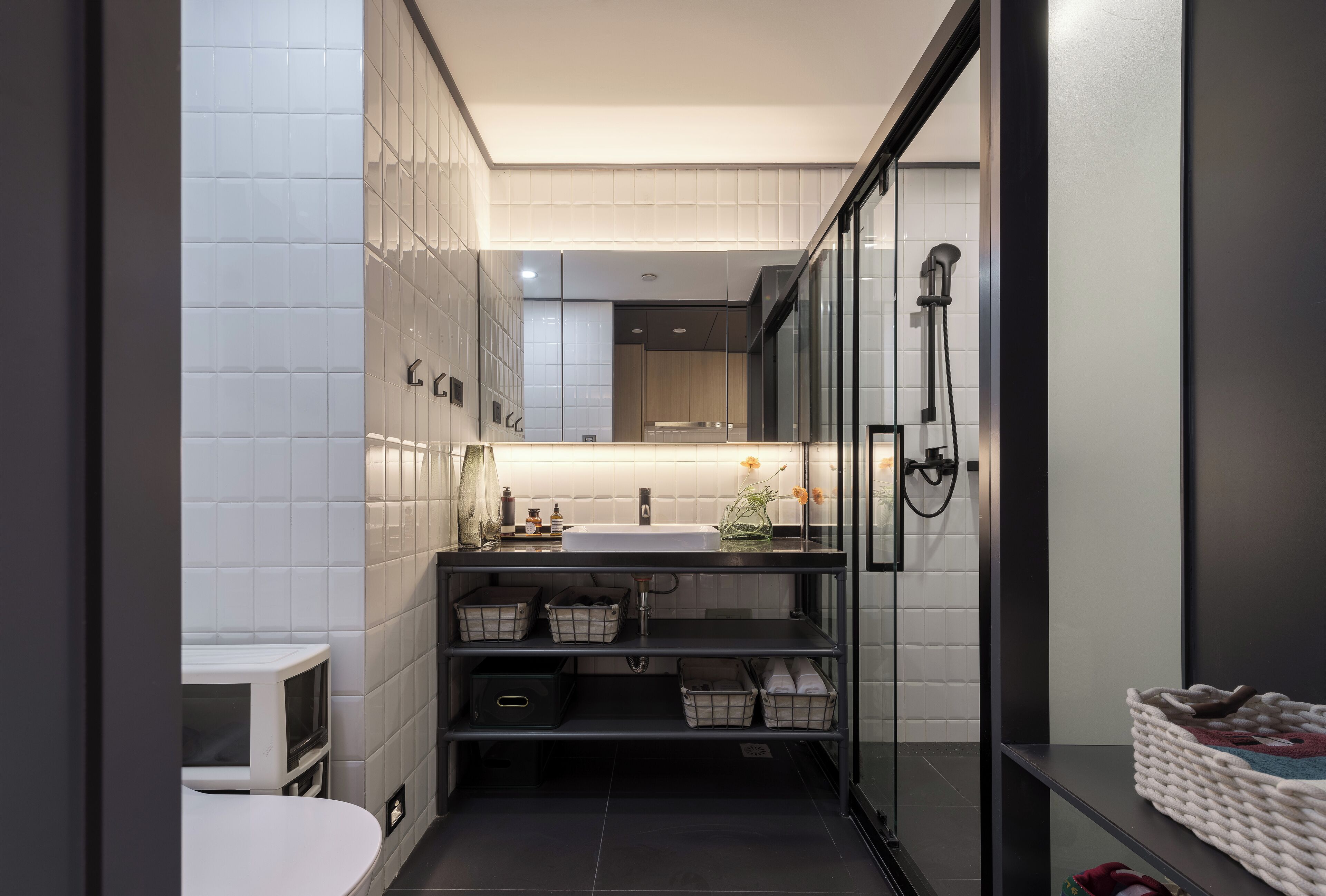 Un baño moderno con cabina de ducha de vidrio, lavamanos blanco y tocador negro.