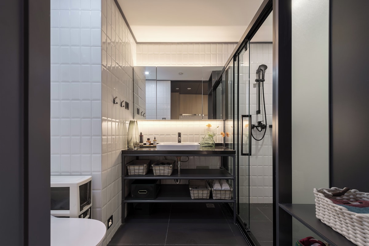 A modern bathroom with a glass shower enclosure, a white sink, and a black vanity.