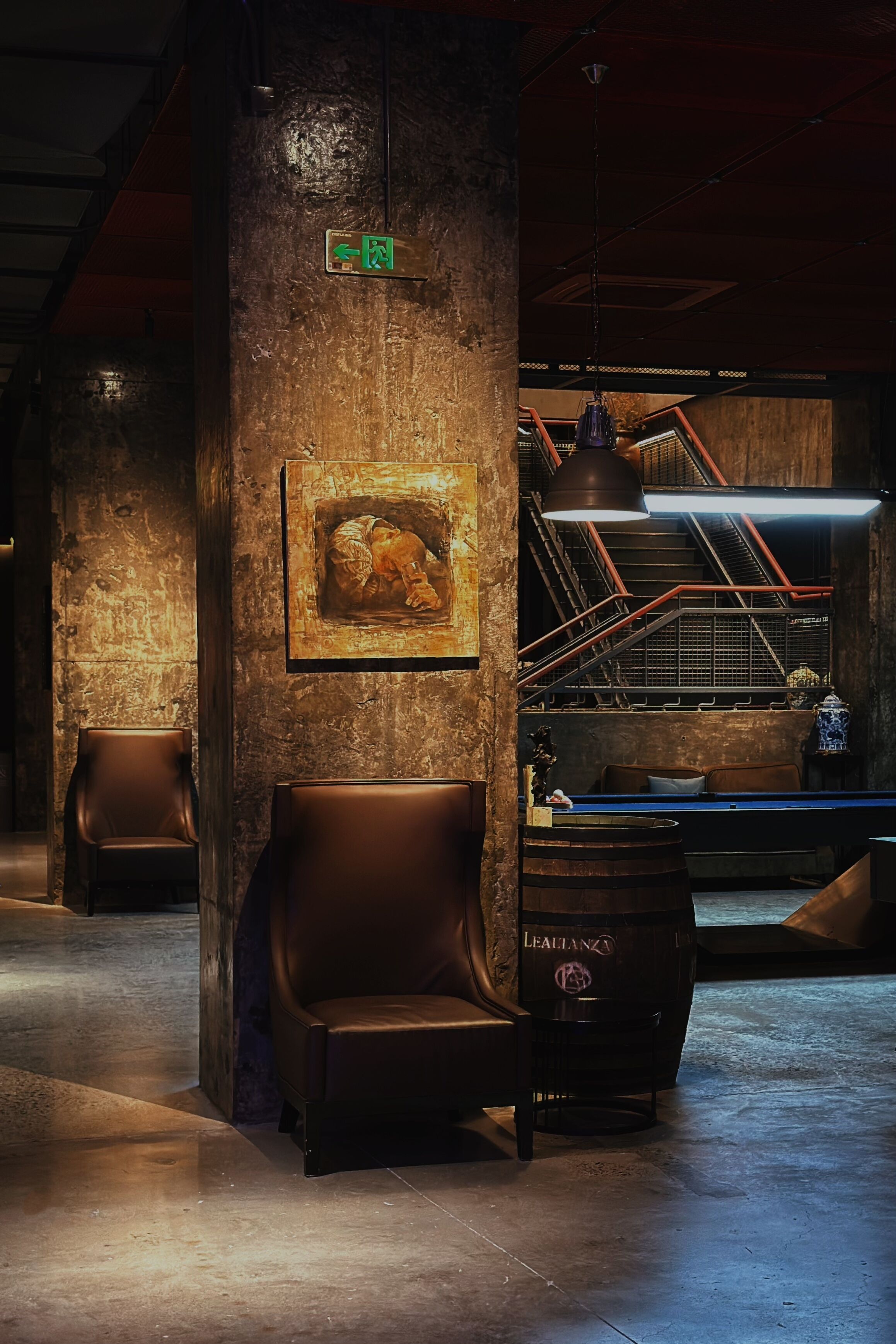 A dimly lit lobby with a staircase, a framed artwork on the wall, and leather seating.