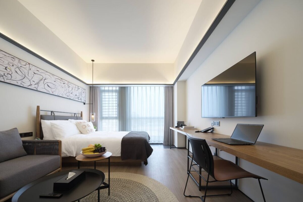 A modern hotel room with a bed, a desk, a laptop, a television, and a sofa.