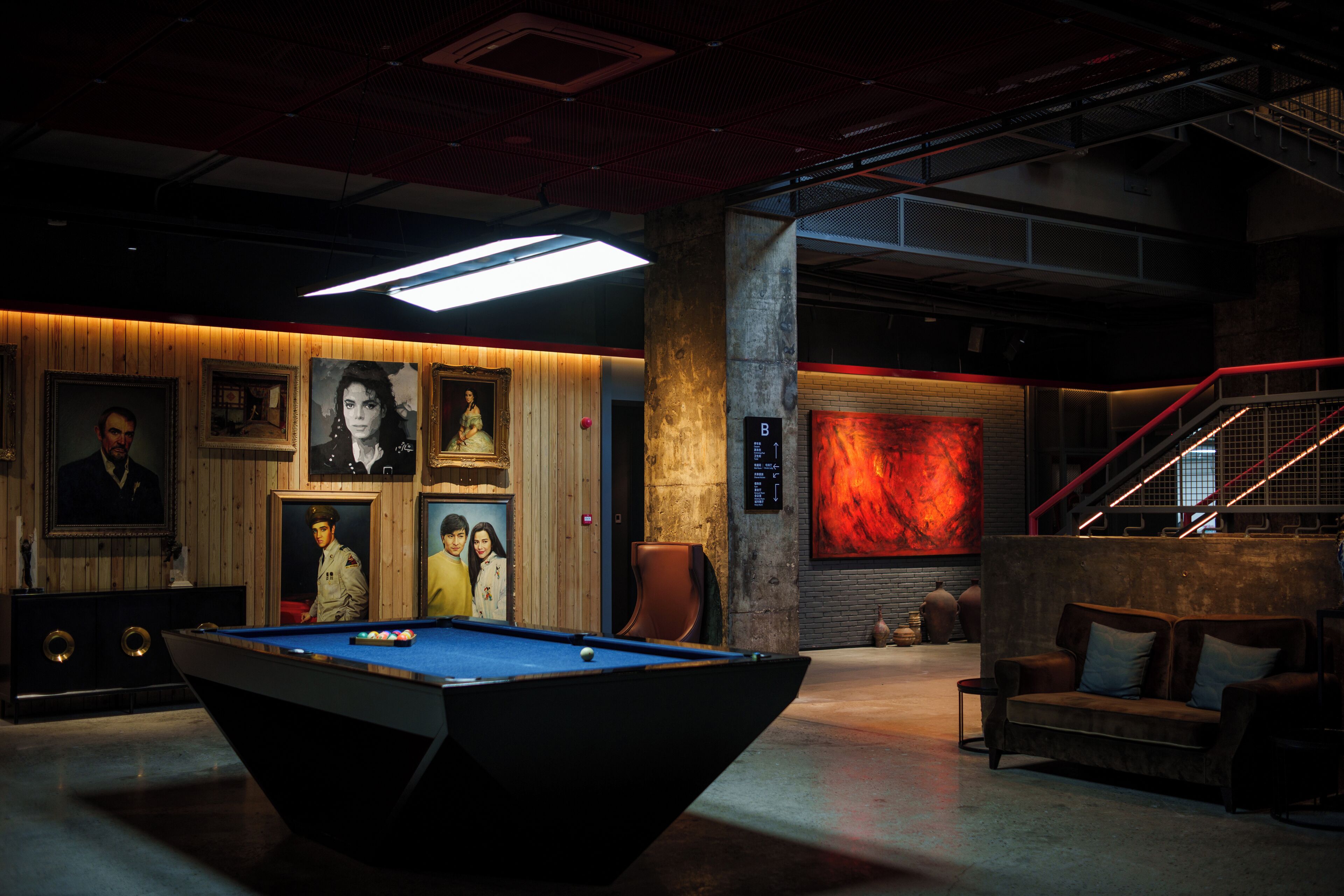 A pool table in a dimly lit room with wooden paneling and framed portraits on the walls.