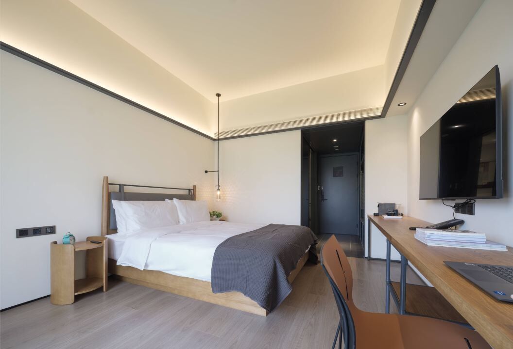 Un dormitorio moderno con cama, mesita de noche, lámpara, escritorio, silla y televisor.