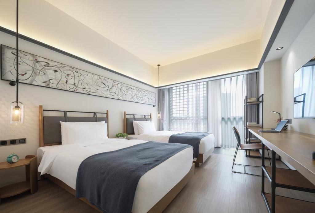 A hotel room with two beds, a desk, and a large window with curtains.
