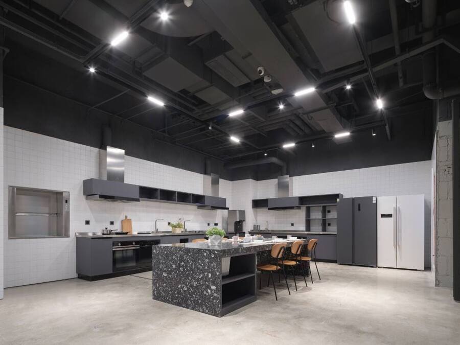 A modern kitchen with a central island, built-in appliances, and a high ceiling with exposed ductwork.