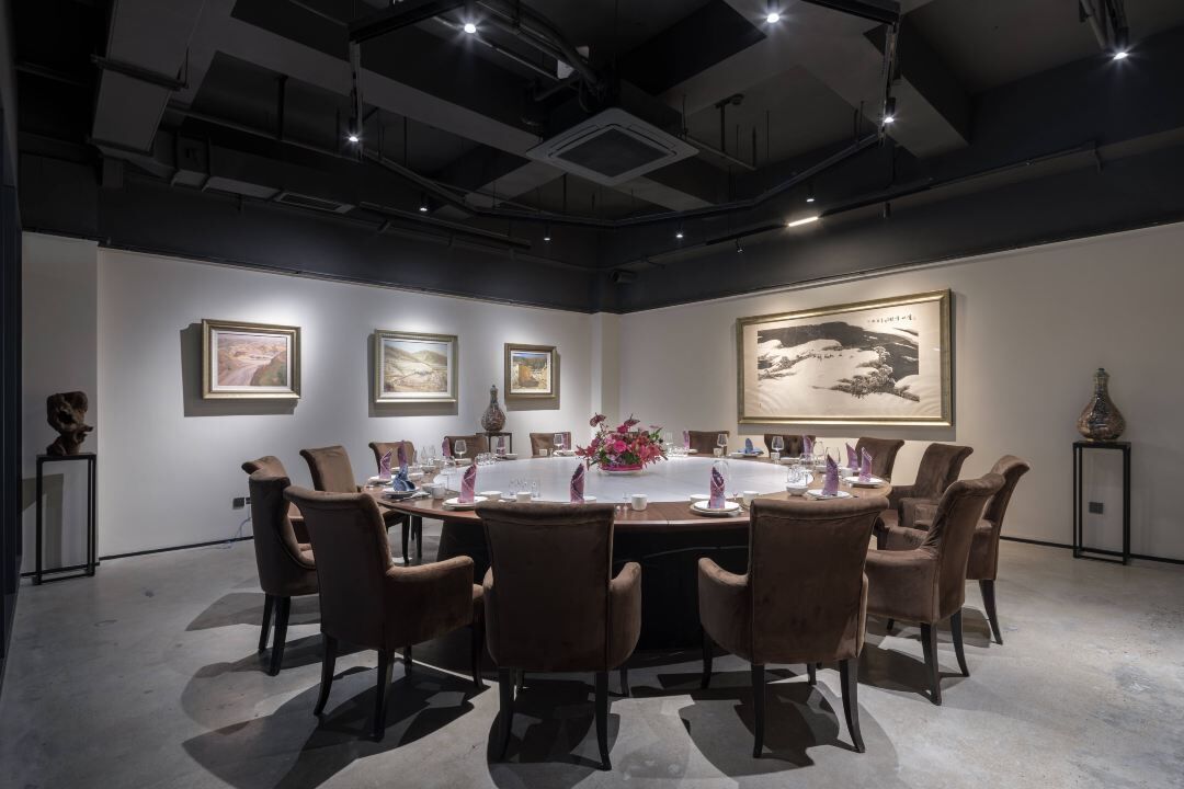 Een vergaderruimte met een ronde tafel, bruine stoelen, ingelijste kunstwerken aan de muren en een groot schilderij boven de tafel.