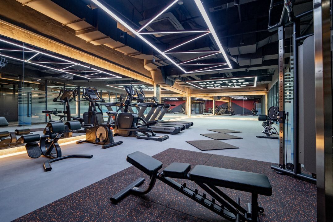 Un gimnasio moderno con varios equipos de ejercicio, como cintas de correr, máquinas de pesas y bancos.