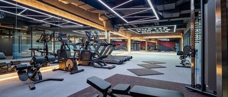 Un gimnasio moderno con varios equipos de ejercicio, como cintas de correr, máquinas de pesas y bancos.