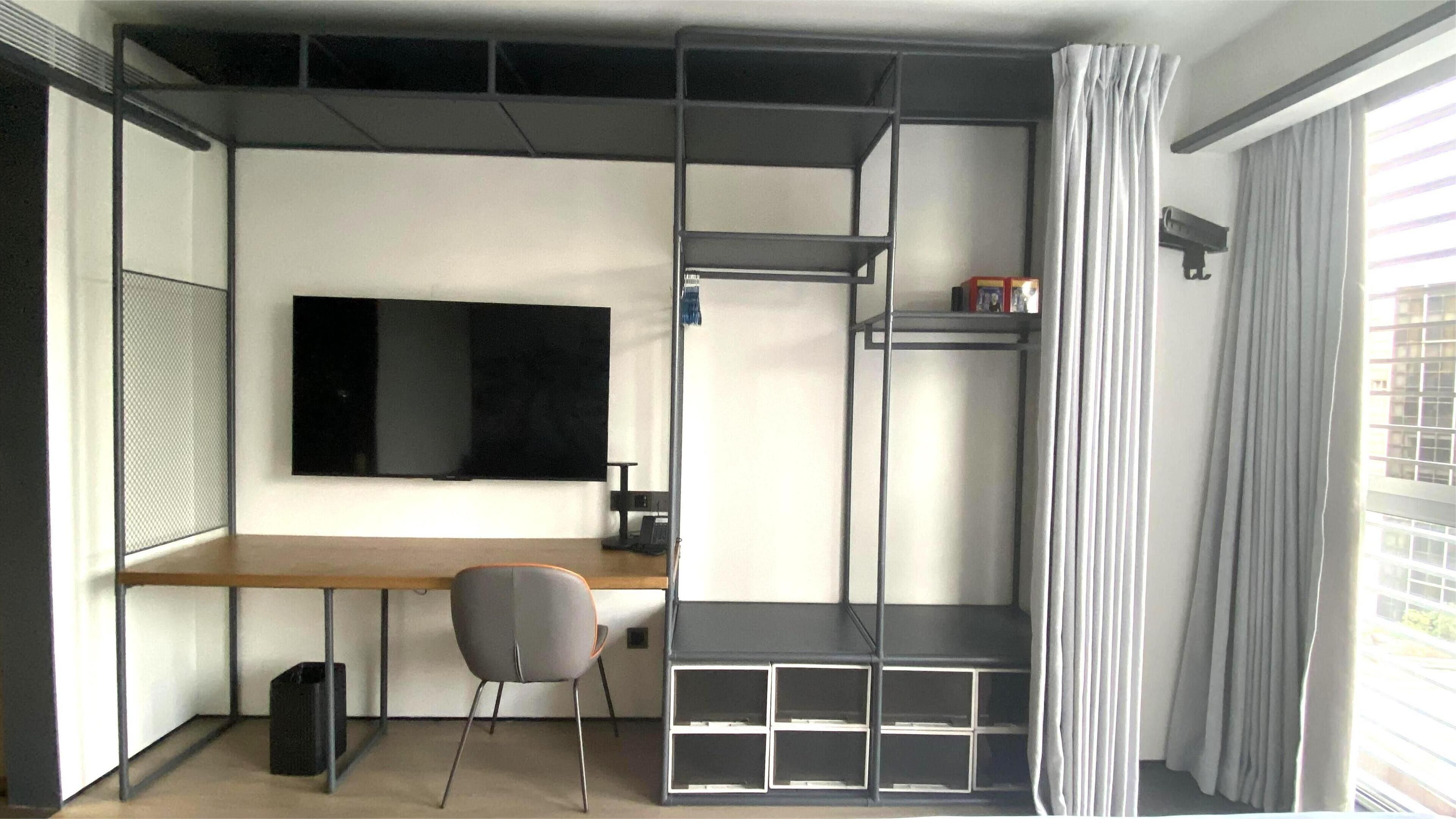 A compact room with a desk, chair, TV, and built-in shelving.