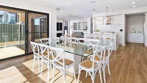 Una cocina moderna con armarios blancos, un refrigerador de acero inoxidable y un comedor con mesa de vidrio y sillas blancas.