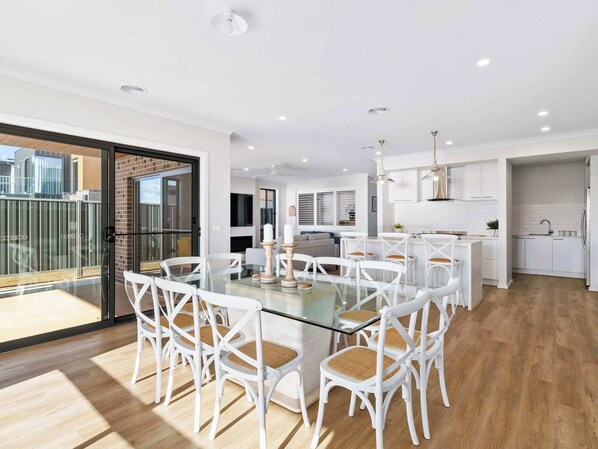 A modern kitchen with white cabinets, a stainless steel refrigerator, and a dining area with a glass table and white chairs.