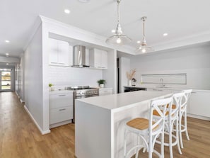 A modern kitchen with white cabinetry, a central island with bar stools, stainless steel appliances, and pendant lighting.