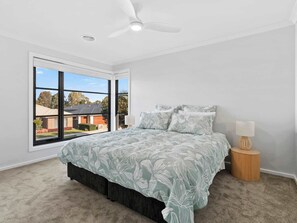 A bedroom with a large window, a bed with floral bedding, a ceiling fan, and a bedside lamp.