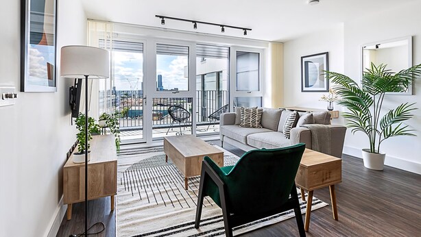 Una sala moderna con sofá, mesa de centro y sillones, un ventanal con vistas a la ciudad y un balcón con mobiliario exterior.