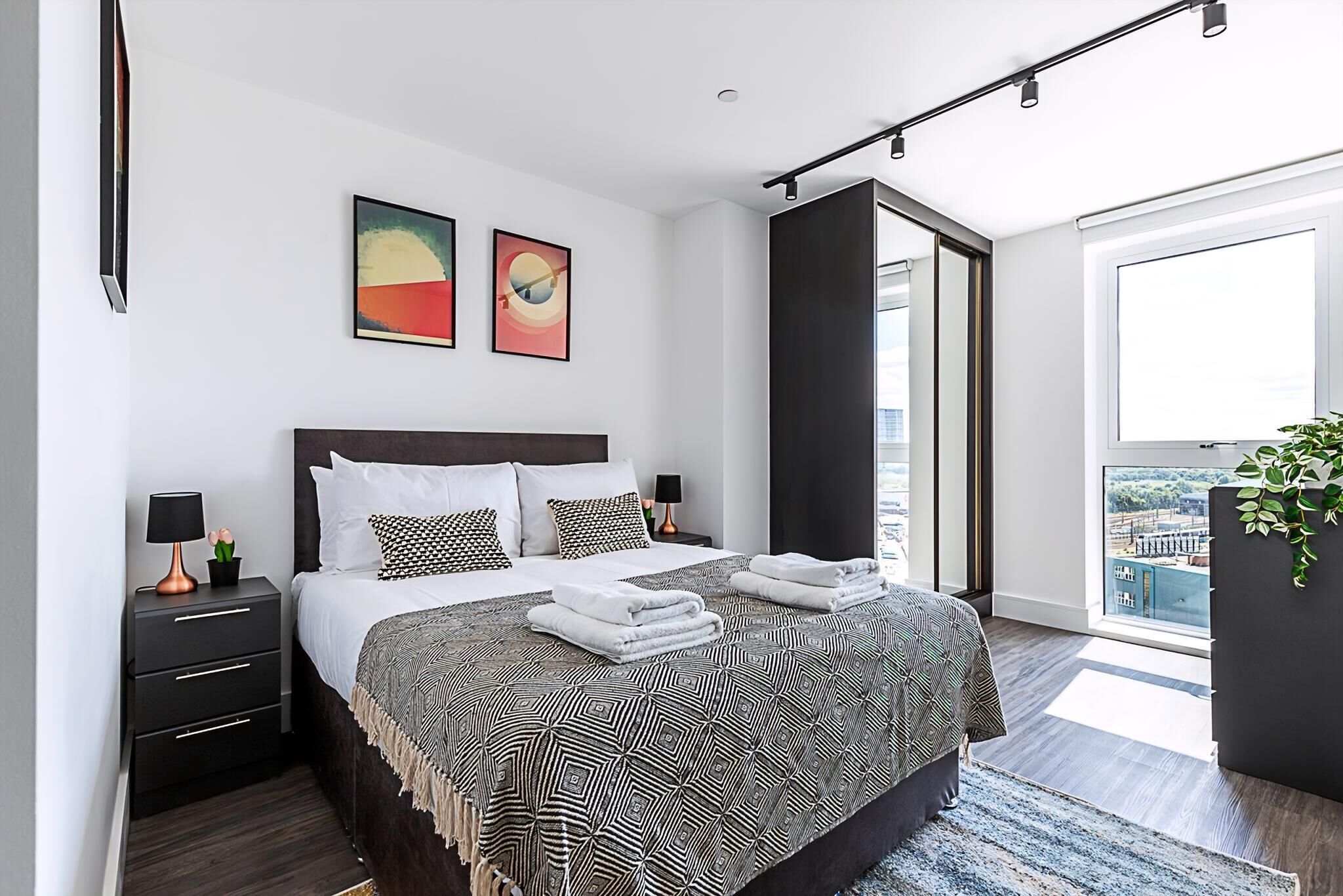 Un dormitorio moderno con una cama grande, dos mesitas de noche y vistas a la ciudad a través de un ventanal.