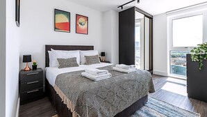 Un dormitorio moderno con una cama grande, dos mesitas de noche y vistas a la ciudad a través de un ventanal.