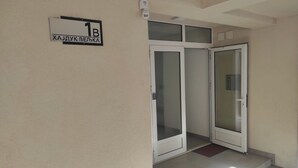 Entrada de un edificio con un letrero que indica la habitación 1B, una puerta de vidrio y una cámara de seguridad.
