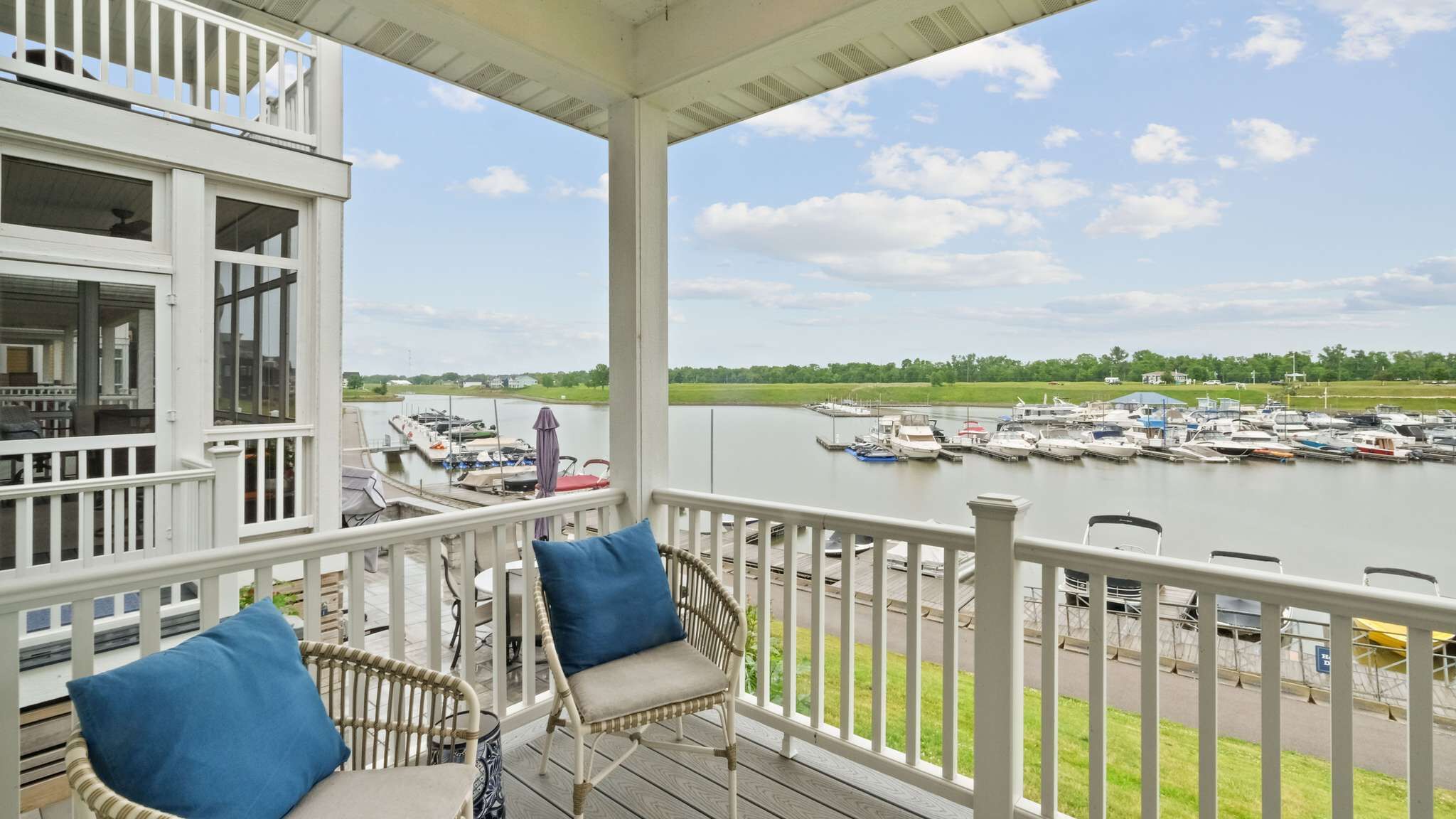 Ein überdachter Balkon mit Korbstühlen und Blick auf eine Marina mit Booten.