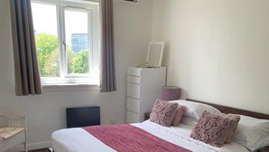 Une chambre à coucher avec un grand lit, une commode, une chaise et une fenêtre avec des rideaux.
