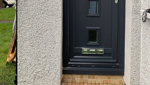 Une porte noire avec un mur à texture, une petite fenêtre et un carillon.
