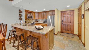 A modern kitchen with wooden cabinets, a stainless steel refrigerator, and a granite countertop. - 2BR Main St Condo, Walk to Ski Lift! (Park City)