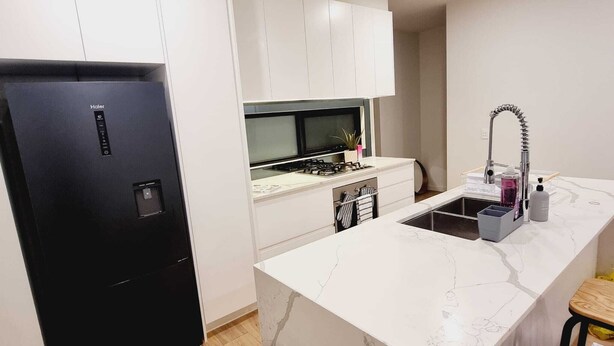 Une cuisine compacte avec un réfrigérateur noir, des armoires blanches, un plan de travail en marbre, un évier et un petit tabouret en bois.