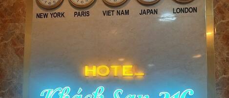 Una pared con relojes mostrando diferentes ciudades y un letrero de neón para Hotel Khach San 31C.