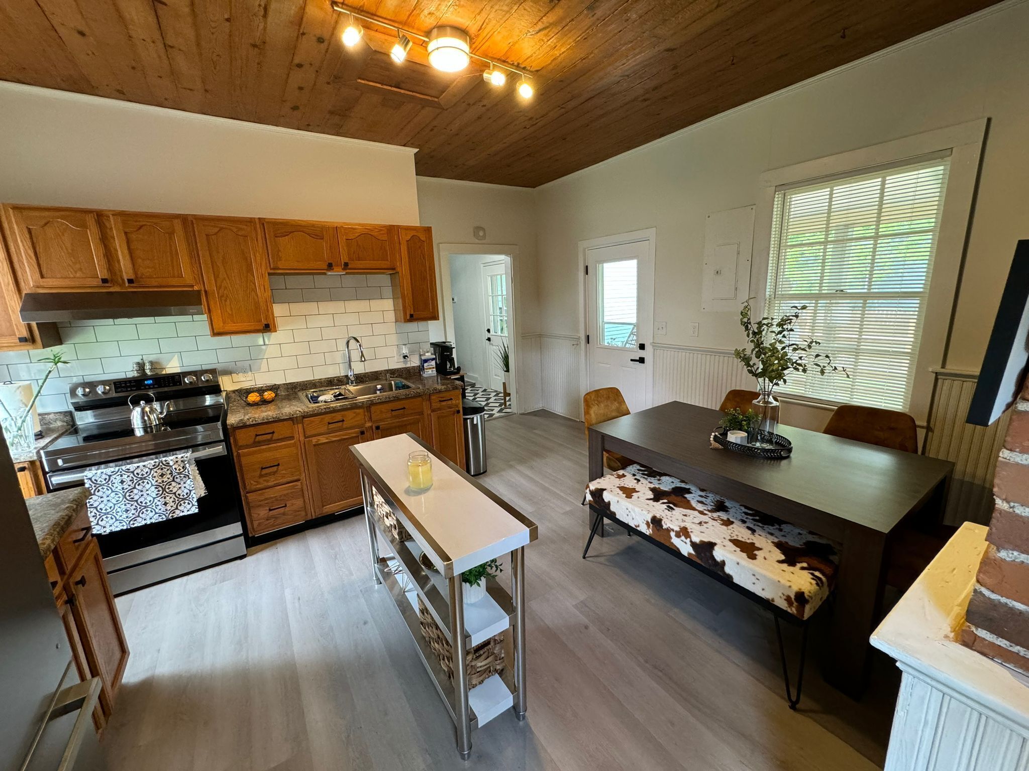 A spacious kitchen with wooden cabinets, a stainless steel stove, and a dining area with a bench and table.