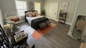 Une chambre à coucher comprenant un lit, des tables de chevet, un ventilateur de plafond, une fenêtre, une porte et une petite table avec un jeu d’échecs.
